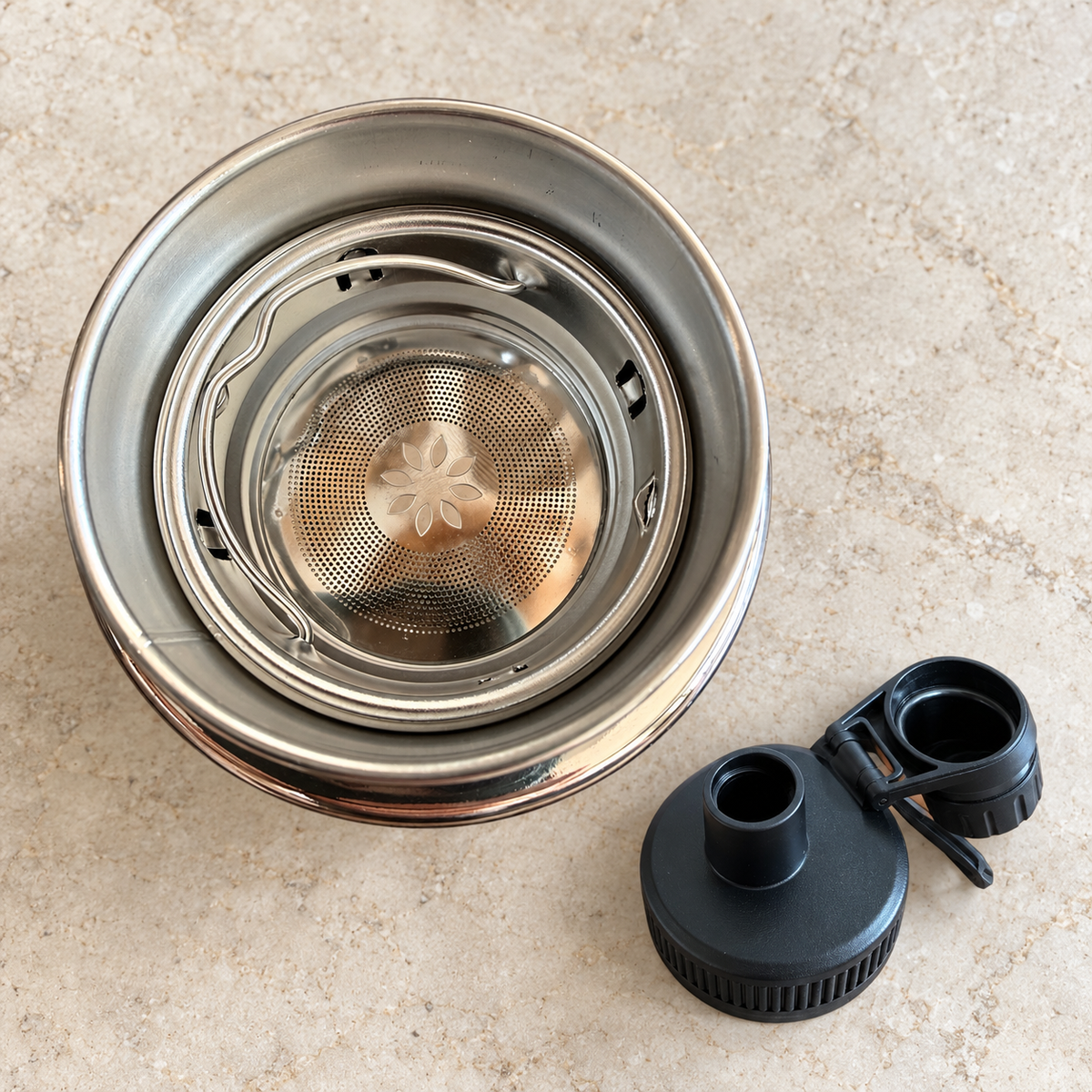 Overhead view of the fitted stainless steel infuser inside the bottle, with the drinking lid beside it
