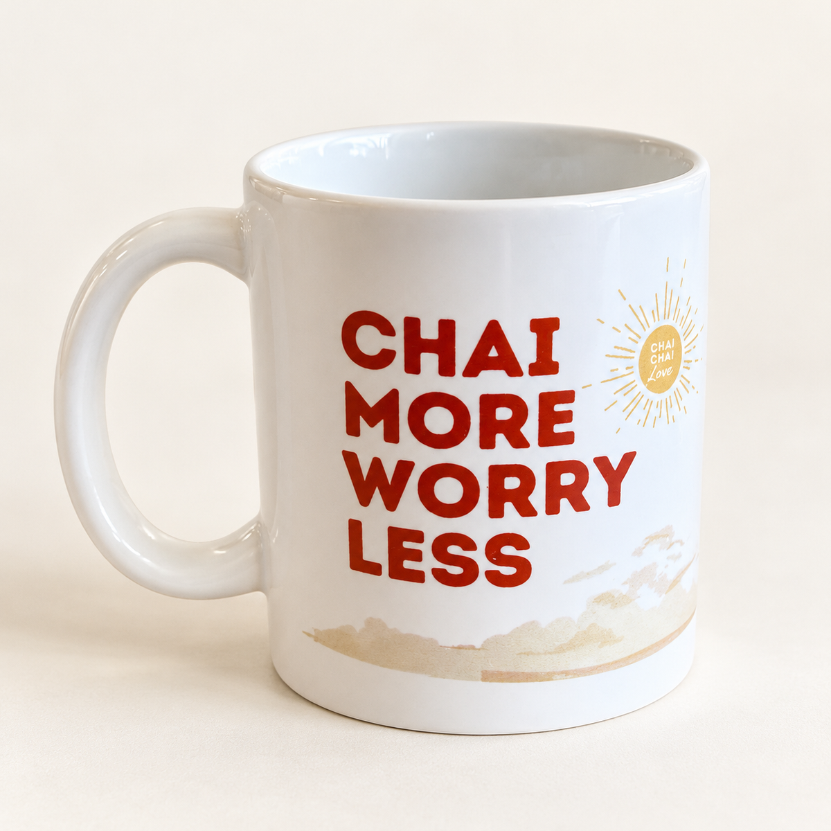 White ceramic Chai More, Worry Less mug with rust-red lettering and gold sun detail